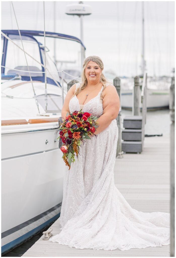 bride wearing a lace dress and holding her bouquet next to a boat in Ohio