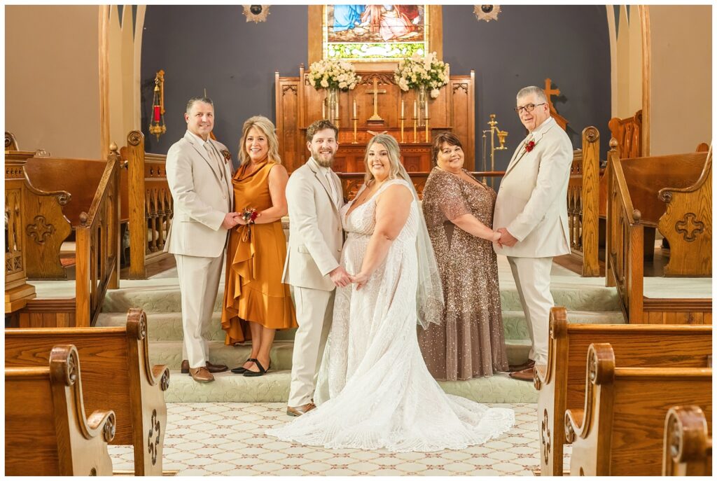 bride and groom posing with both sets of parents at the stairs inside the church