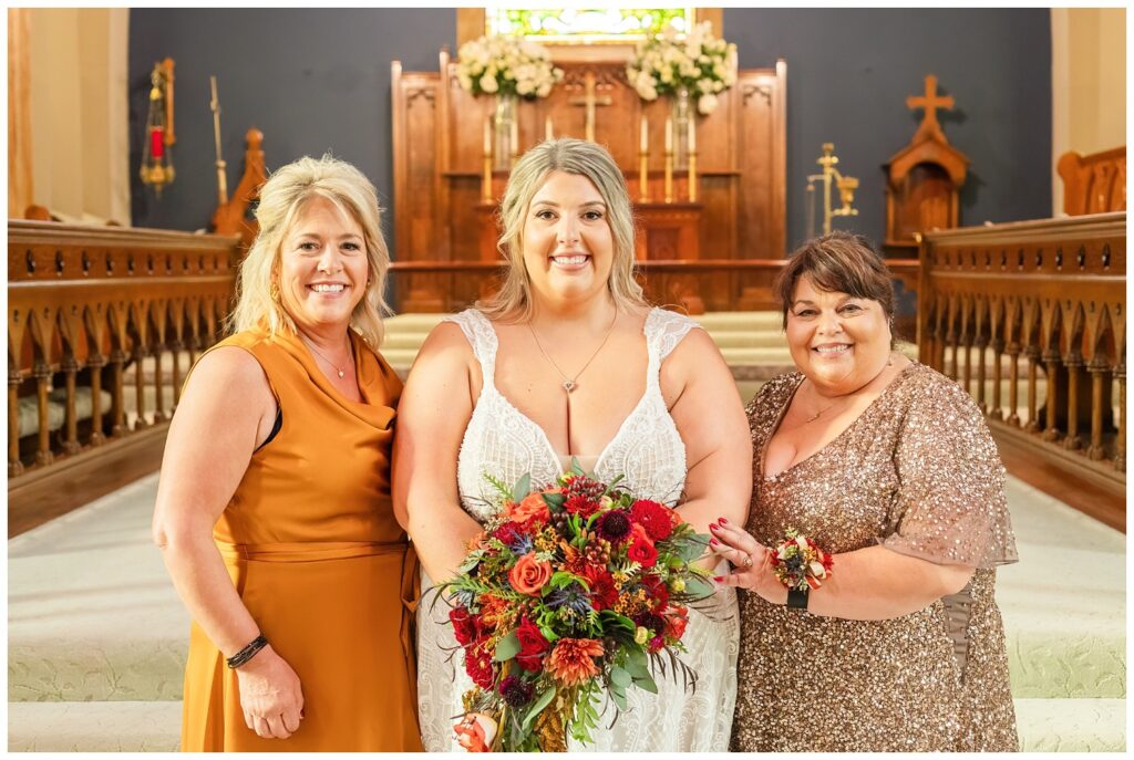 both the bride's mom and groom's mom posing with the bride at the church