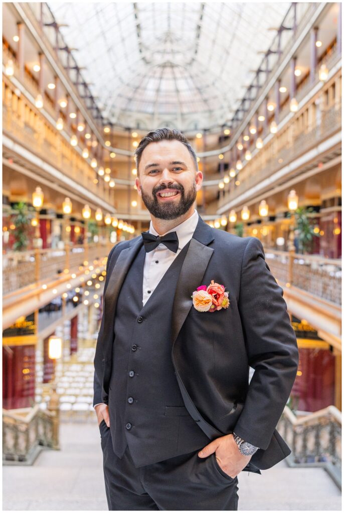 groom posing with hands in his pockets wearing an orange and pick boutonniere 