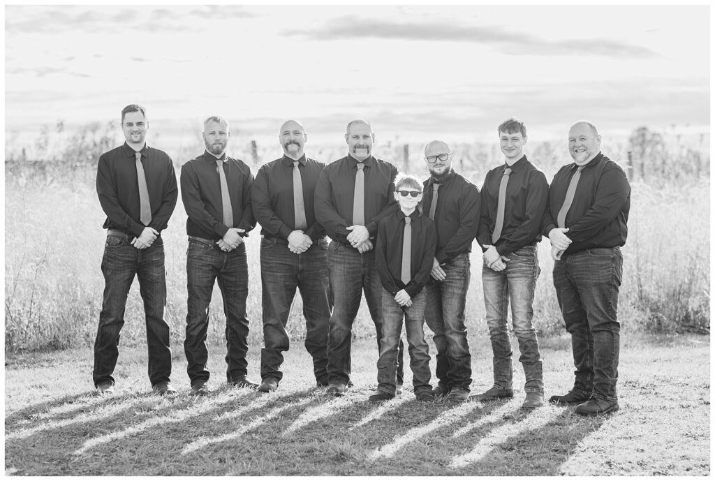 groomsmen posing in front of a large field outside with the ring bearer 