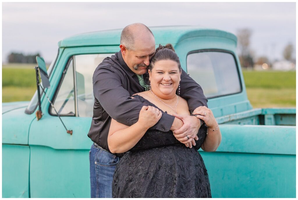 groom hugging the bride from behind  next to an old teal green truck on the property at Pickwick Place