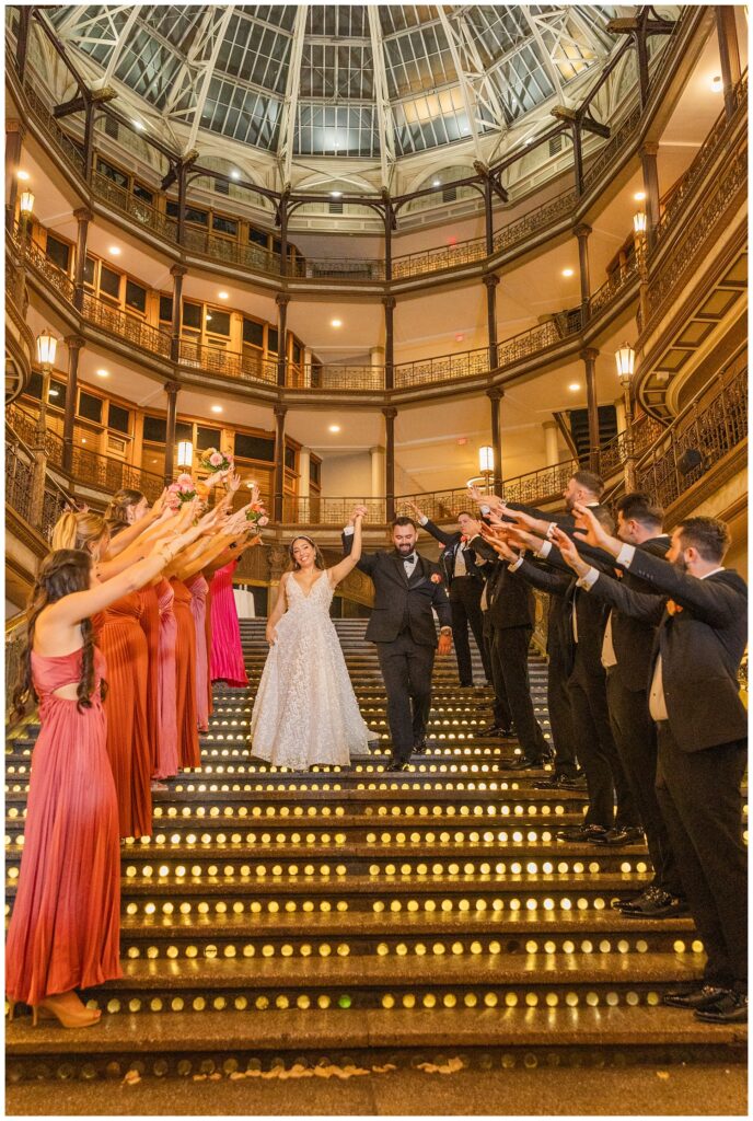 bride and groom walking down the stairs cheered on by the wedding party 