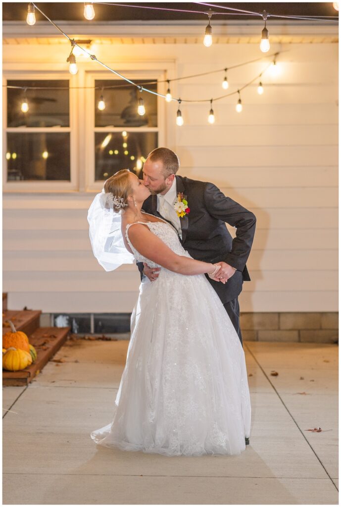 groom dipping the bride back for a kiss on their backyard patio with strung lights