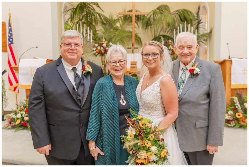 bride posing with her dad and grandparents in front of the altar after the ceremony