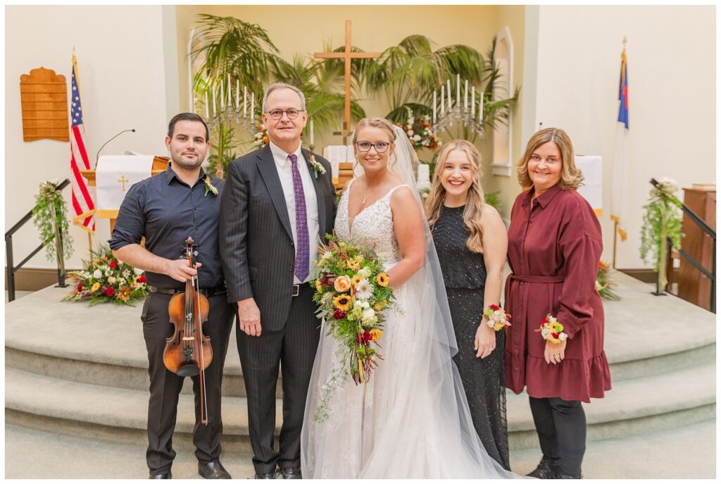 bride posing with the violinist and wedding assistants in front of the altar after the ceremony