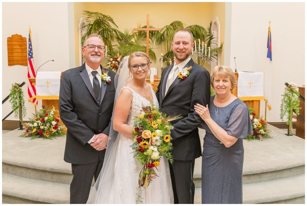 bride and groom posing with the groom's parents after the church ceremony