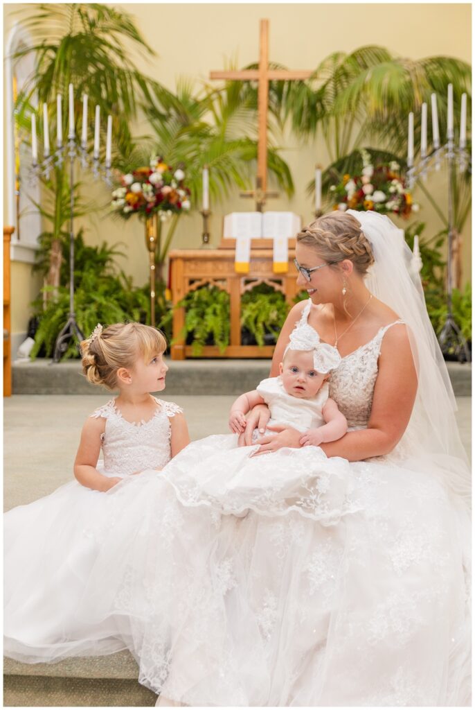 bride posing with her flower girl and a baby on the steps of the altar 