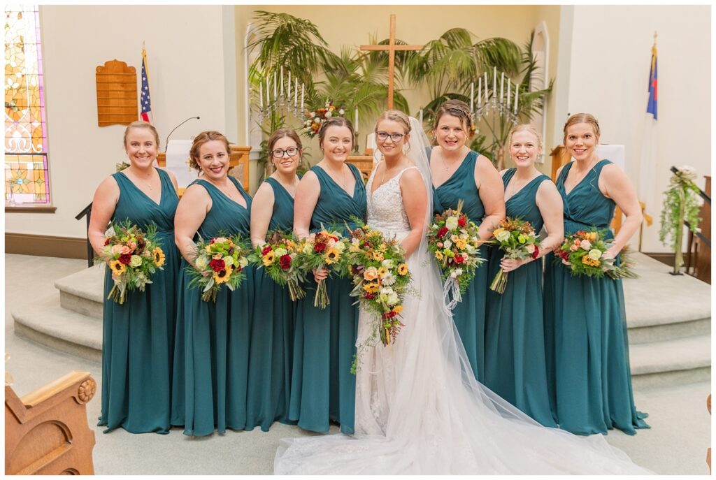 bride posing with her bridesmaids who are wearing green emerald dresses