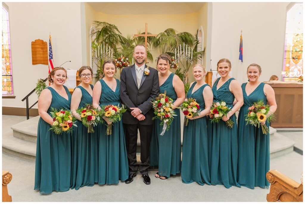 groom posing with the bridesmaids at the church before the ceremony