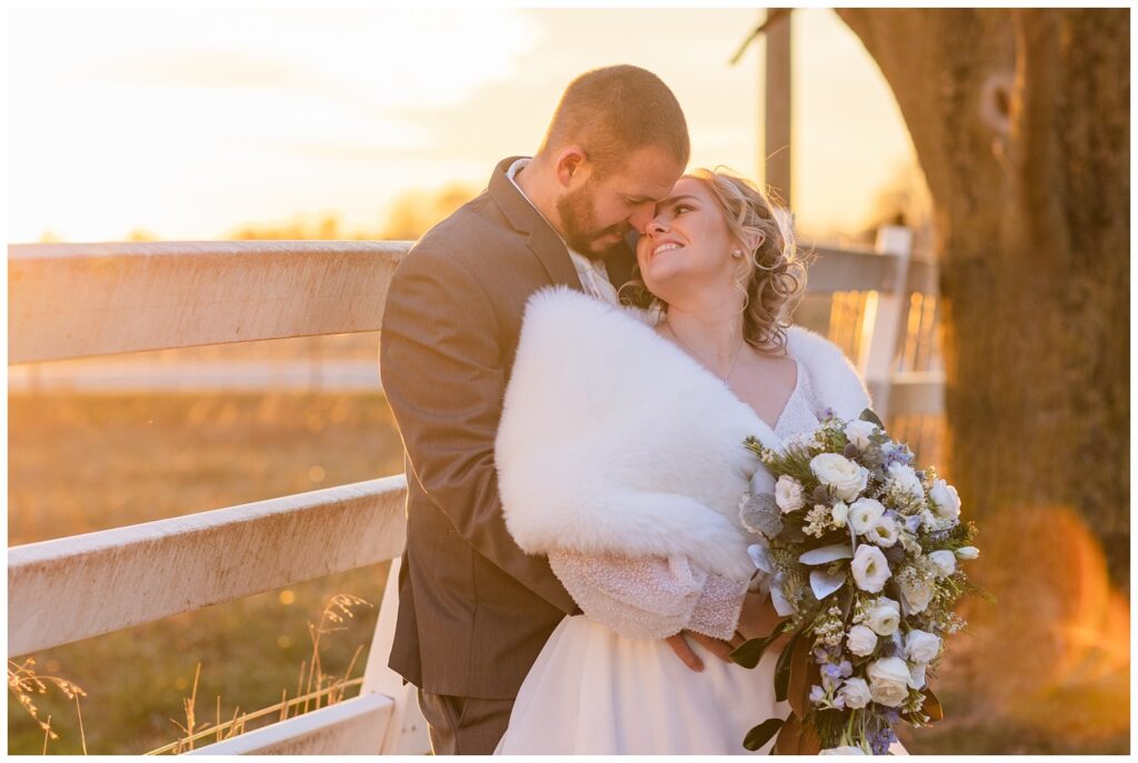 groom holding the bride next to a white fence at sunset in Fremont, Ohio