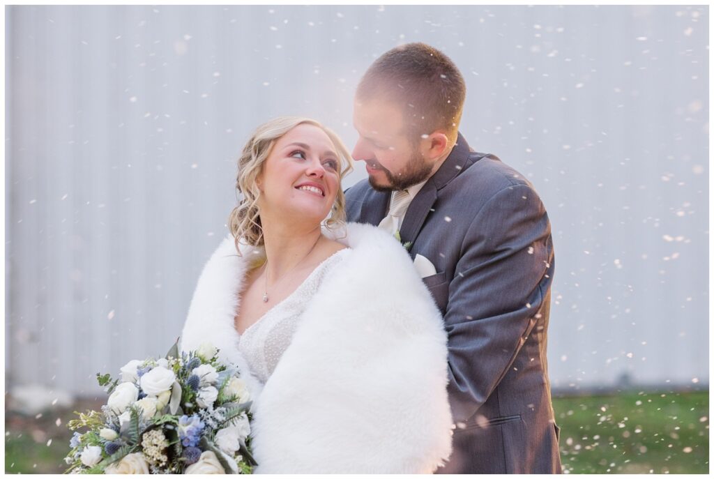 groom holding the bride from behind as snow is falling