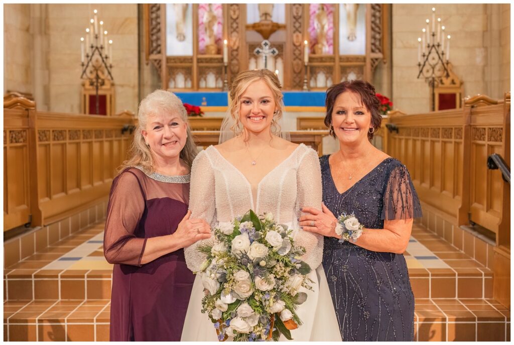 bride posing with her mom and groom's mom at the church altar