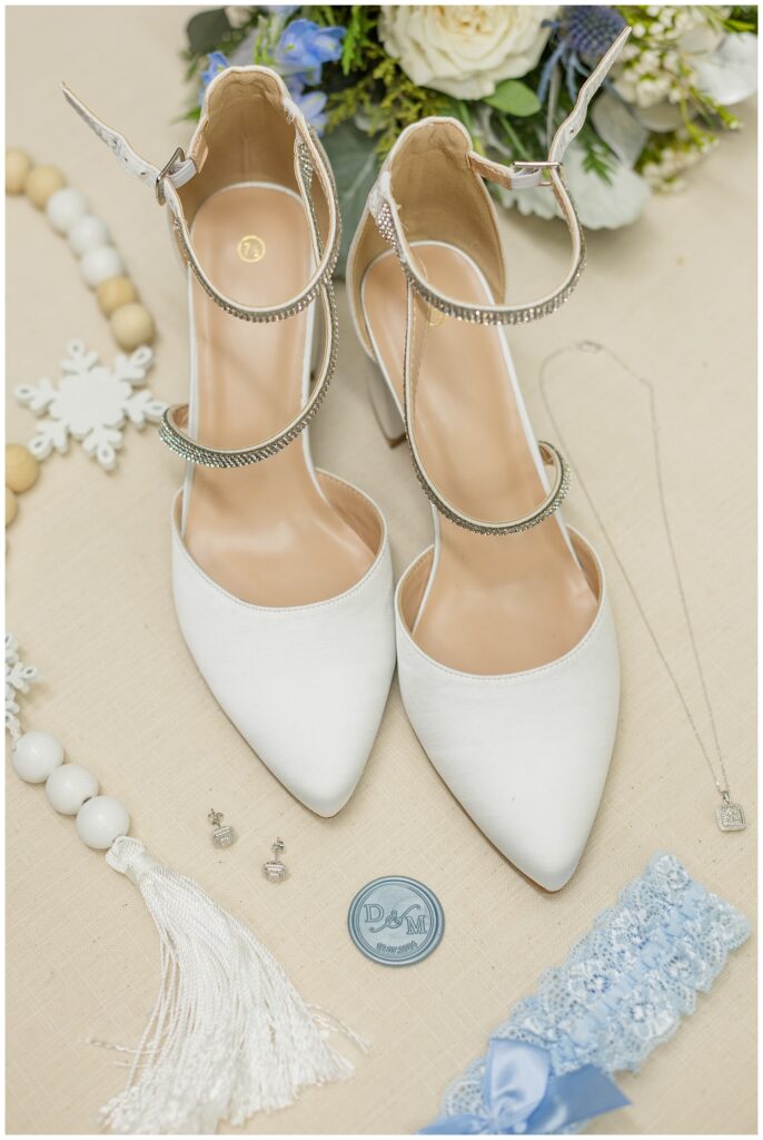 bride's white and crystal wedding shoes sitting on a beige mat with jewelry