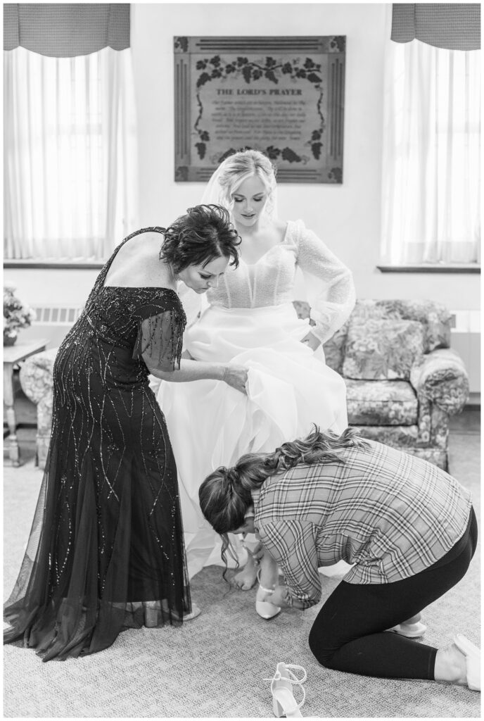 bride's mom and one of the bridesmaids helping the bride get on her shoes