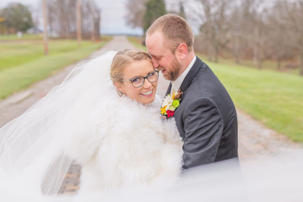 wedding couple wrapped in the bride's  veil while posing on a brick road