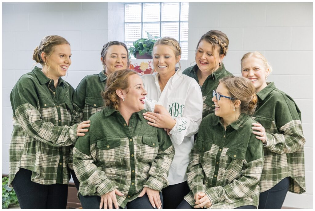 bride wearing a white decorated shirt with wedding date and initials while surrounded by the bridesmaids