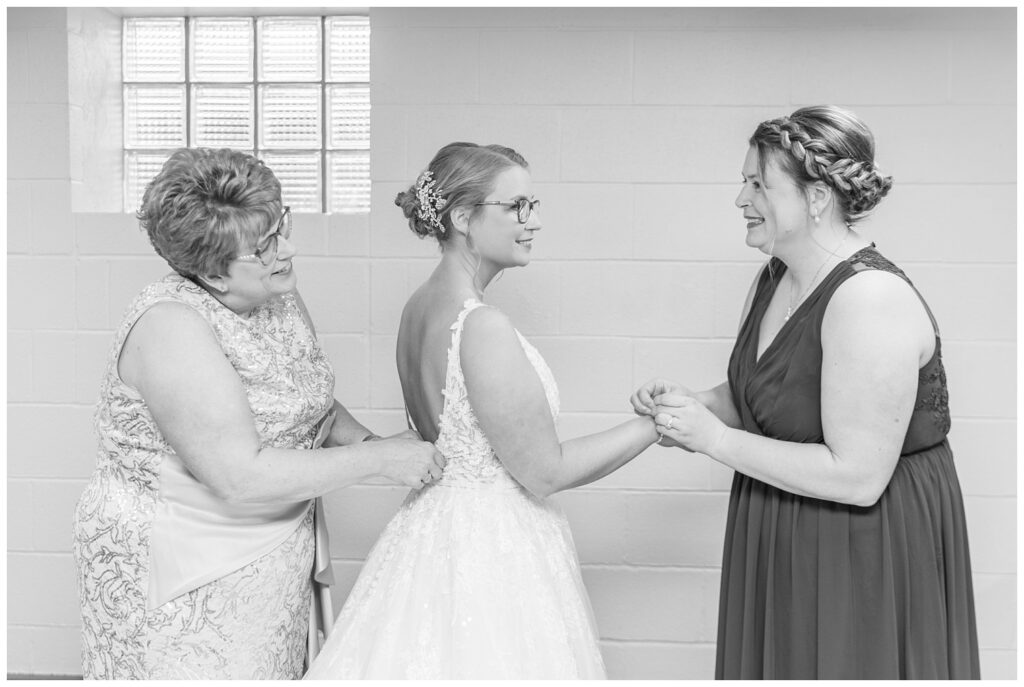 bride's mom zipping up her dress while her sister puts on her bracelet 