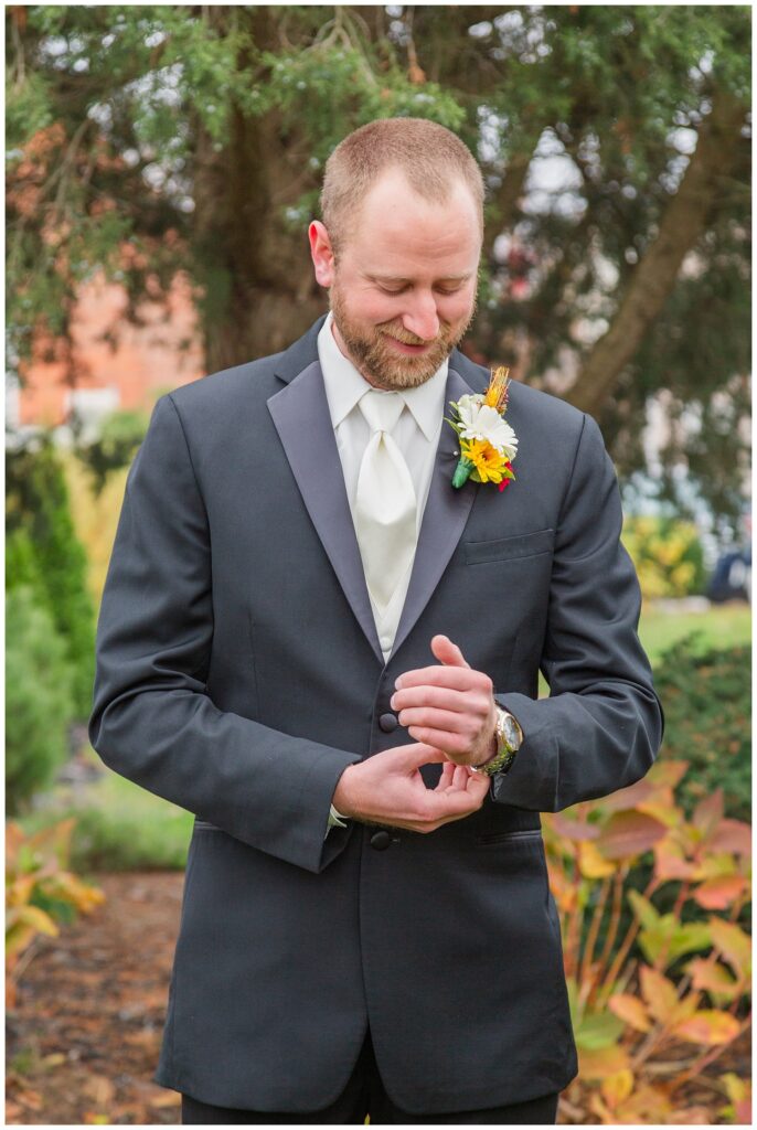 groom wearing a dark suit with white shirt and ivory tie checking his watch