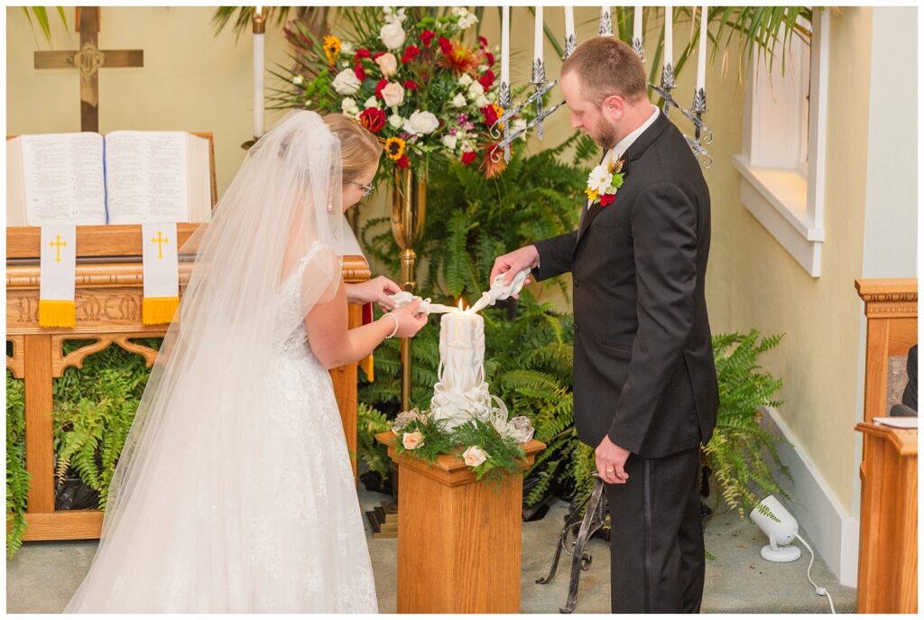 bride and groom lighting candle during fall church ceremony 