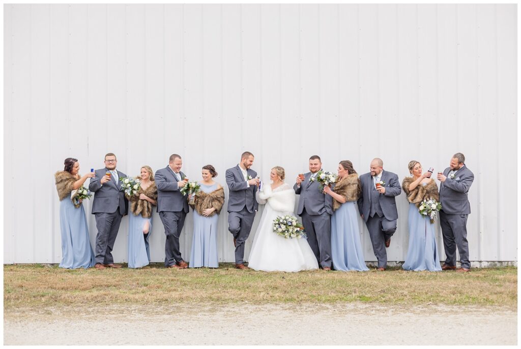 wedding party toasting with beers while posing on the bride's family farm