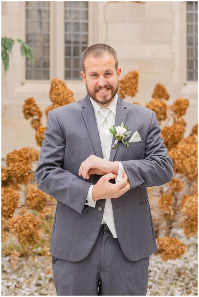 groom adjusting his cufflinks wearing a gray suit with a white shirt and tie