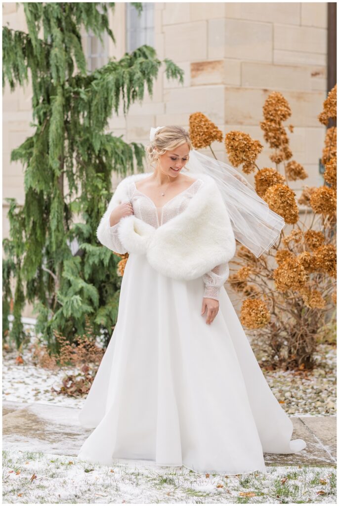 bride holding the side of her shawl with her veil blowing behind her outside