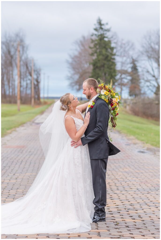 bride and groom facing each other on a brick road with the bouquet behind the groom's head