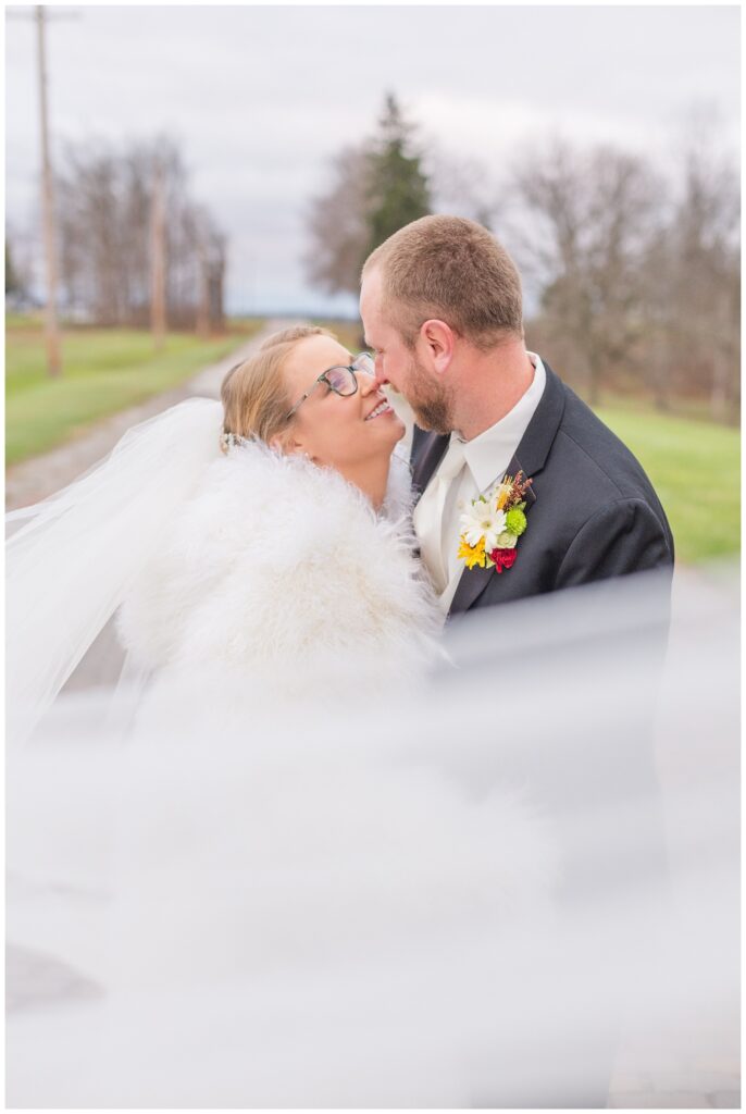 bride and groom holding each other on a brick road while the bride's veil wrapped around