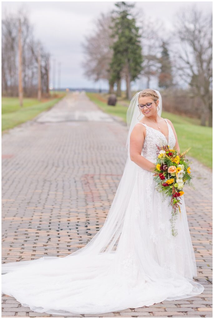 bride looking down at her shoulder and holding her bouquet standing on a brick road