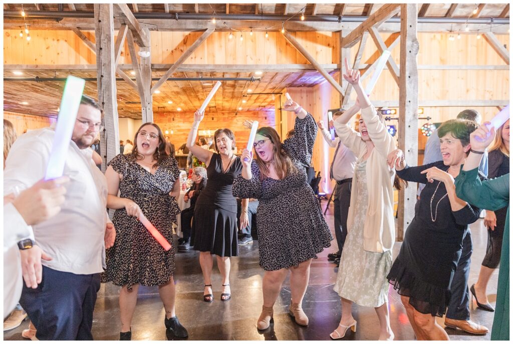 wedding guests posing and dancing with light-up foam wands at the Village Barn venue