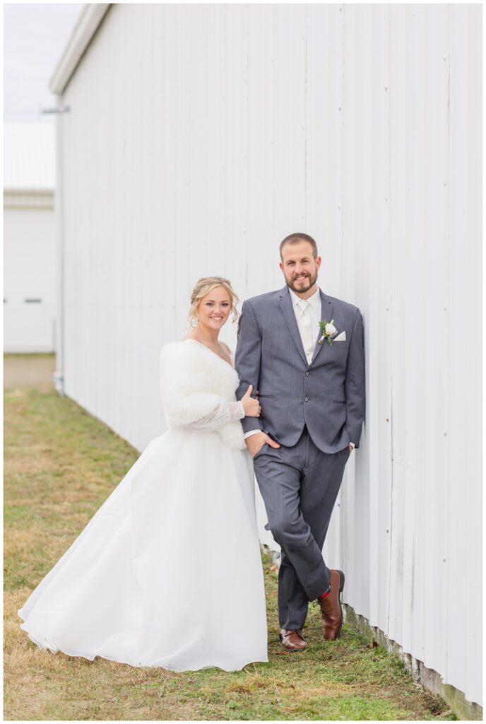 wedding couple posing against a white barn on the bride's family farm