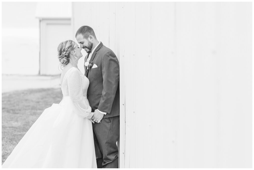 bride and groom holding hands and posing against a white barn in Fremont, Ohio