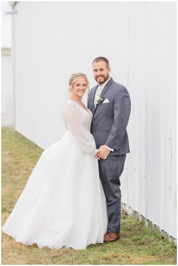 bride and groom holding hands and posing against a white barn in Fremont, Ohio