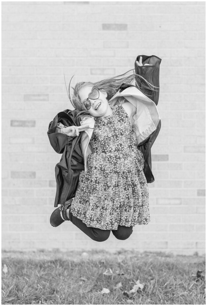 girl wearing heart sunglasses and jumping in the air wearing a graduation gown