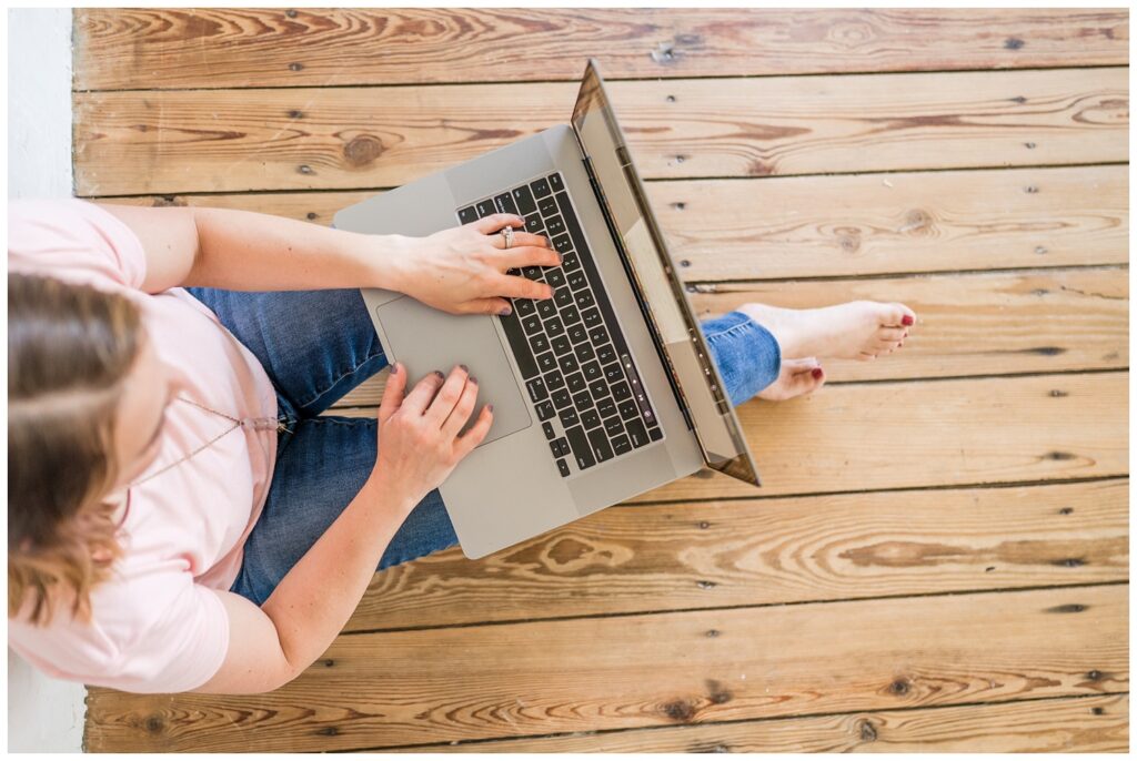 Tiffin, Ohio photographer sitting on a wood floor typing on her laptop