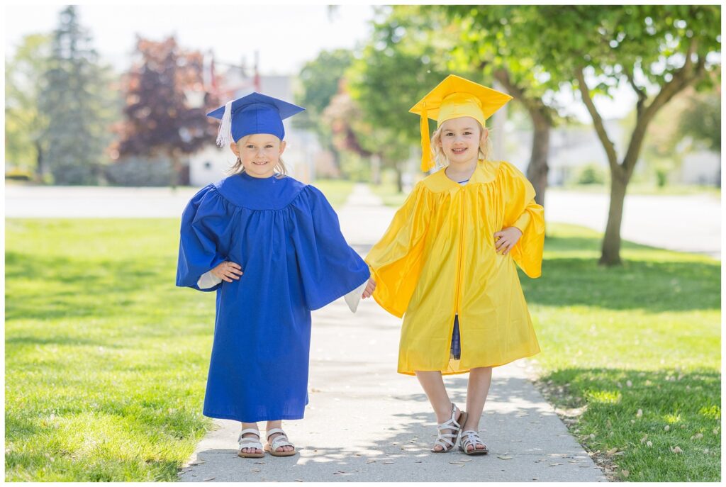 two small girls wearing blue and yellow graduation gowns at mini session