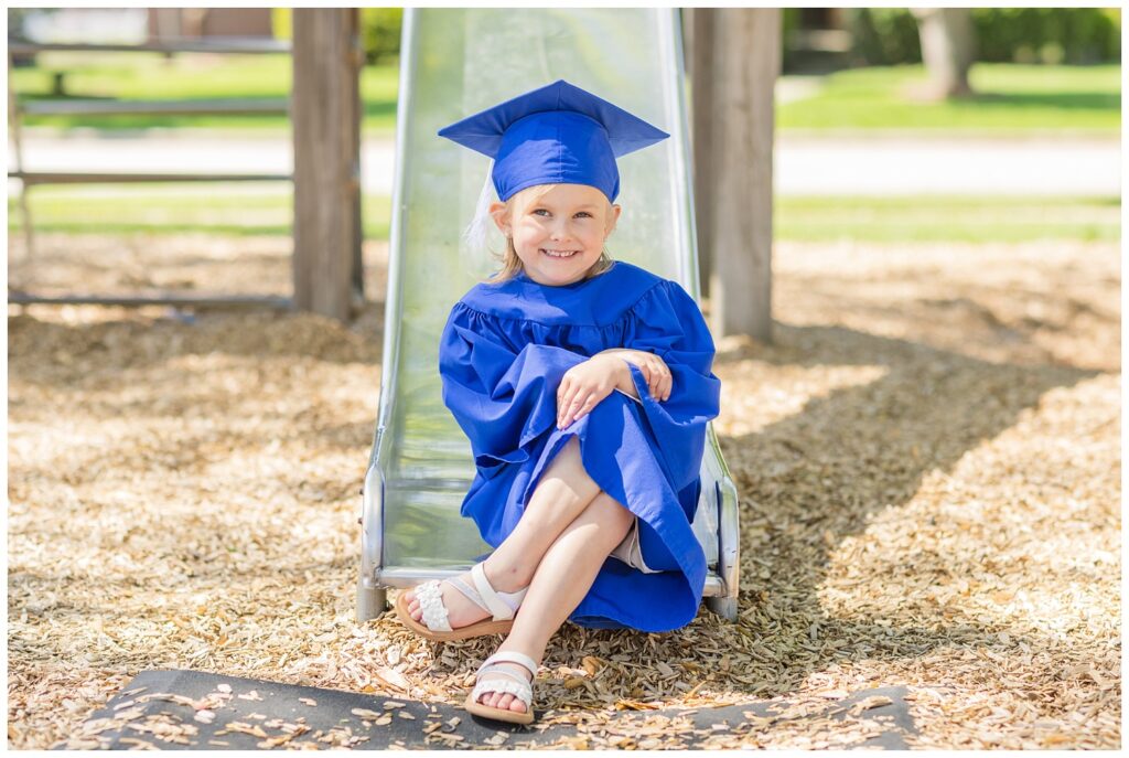 preschool graduate wearing a blue gown sitting on a slide