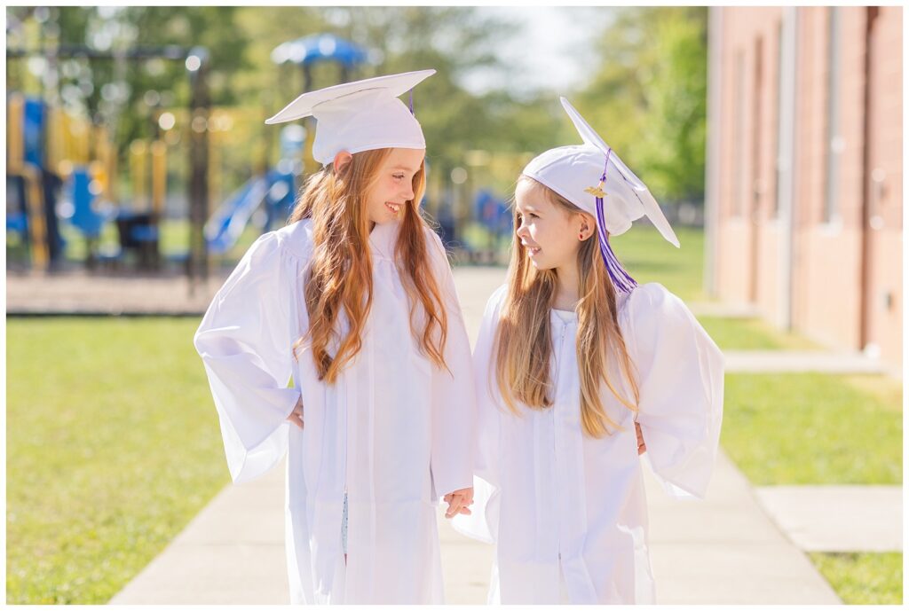 two small girls holding hands and wearing white gowns for graduation mini session