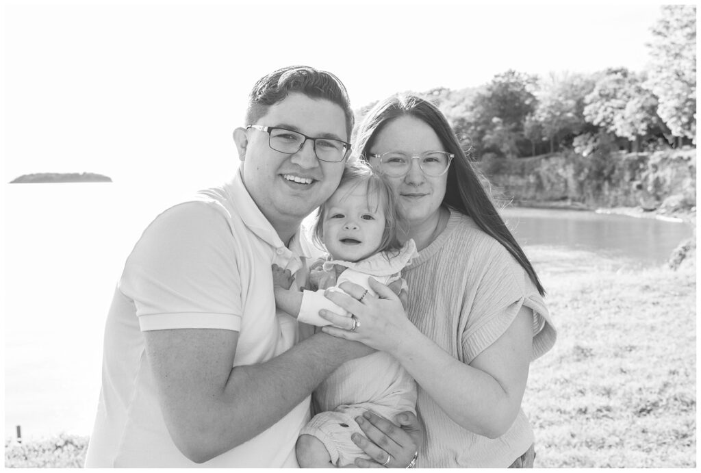 husband and wife hugging their daughter and posing on the grass at Lake Erie 