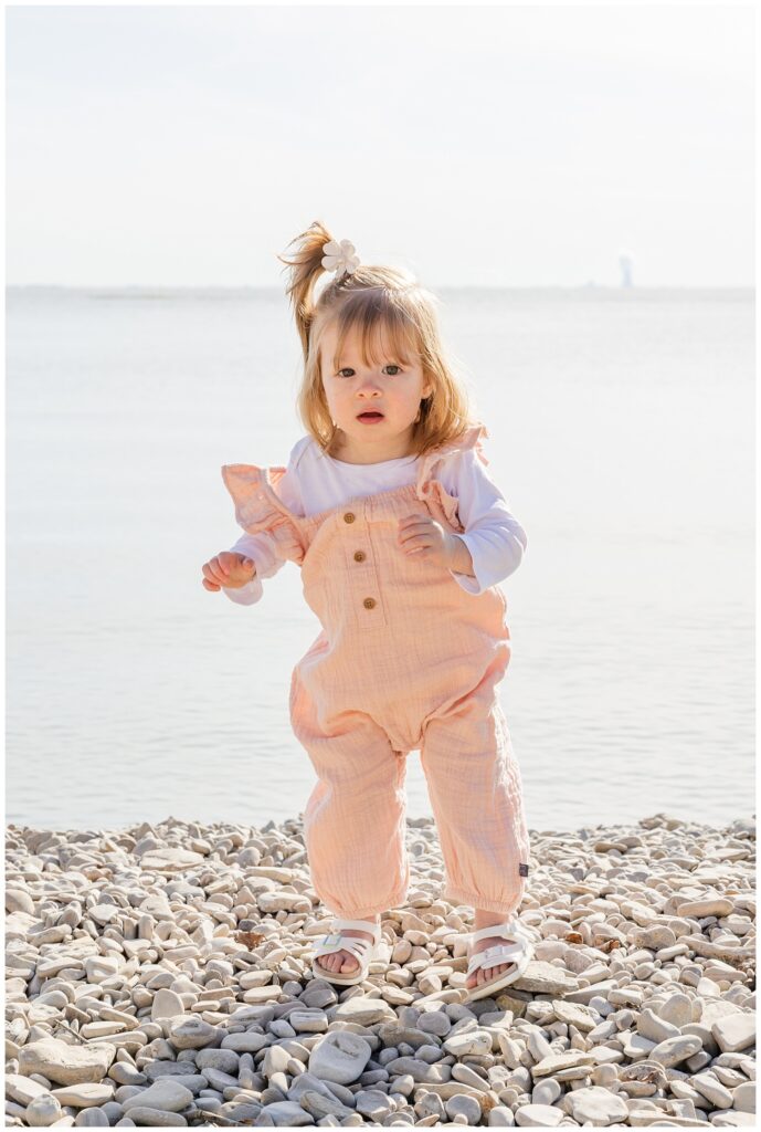 little girl wearing a pink jumpsuit and posing on the rocky beach at Lake Erie family session