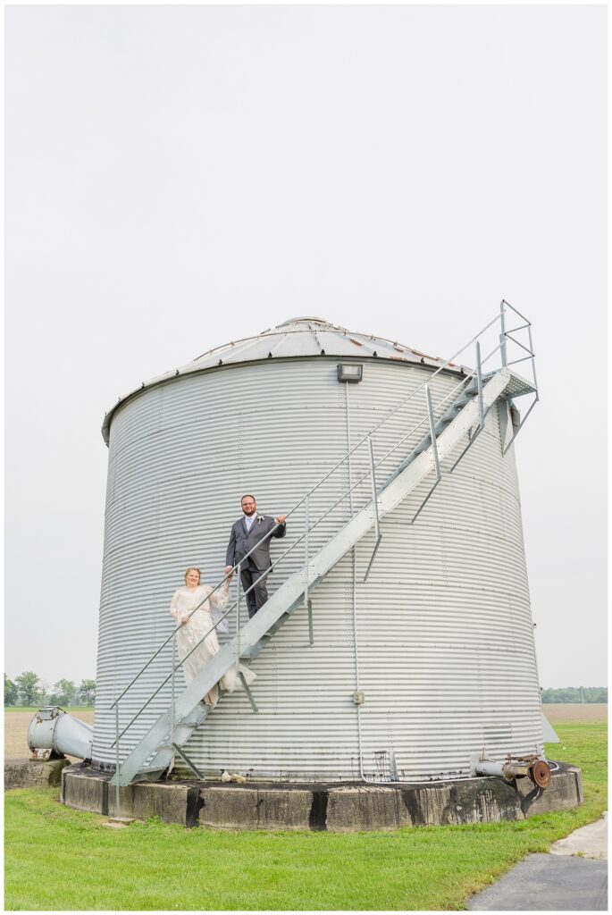 wedding couple posing on the stairs of a grain bin at family farm in Risingsun, Ohio