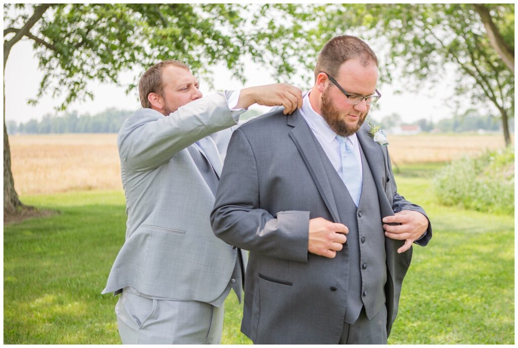 groom's best man helping the groom adjust his jacket from behind outside