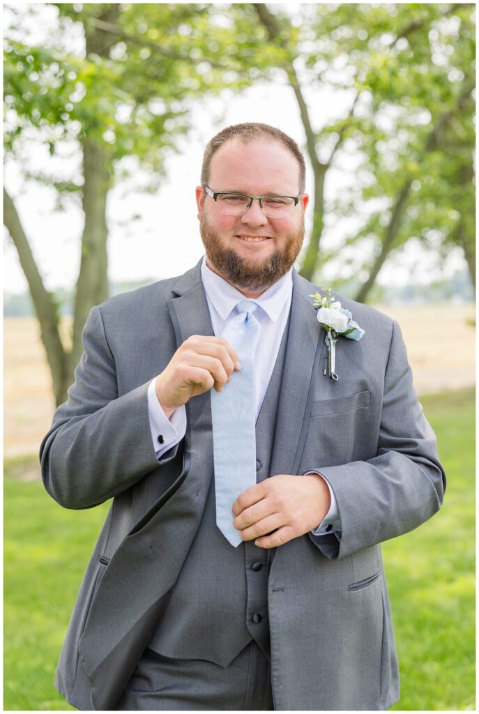 groom adjusting his tie while posing in the backyard of his Risingsun, Ohio home