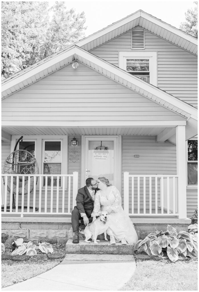 bride and groom share a kiss while holding their dog at their Risingsun, Ohio home
