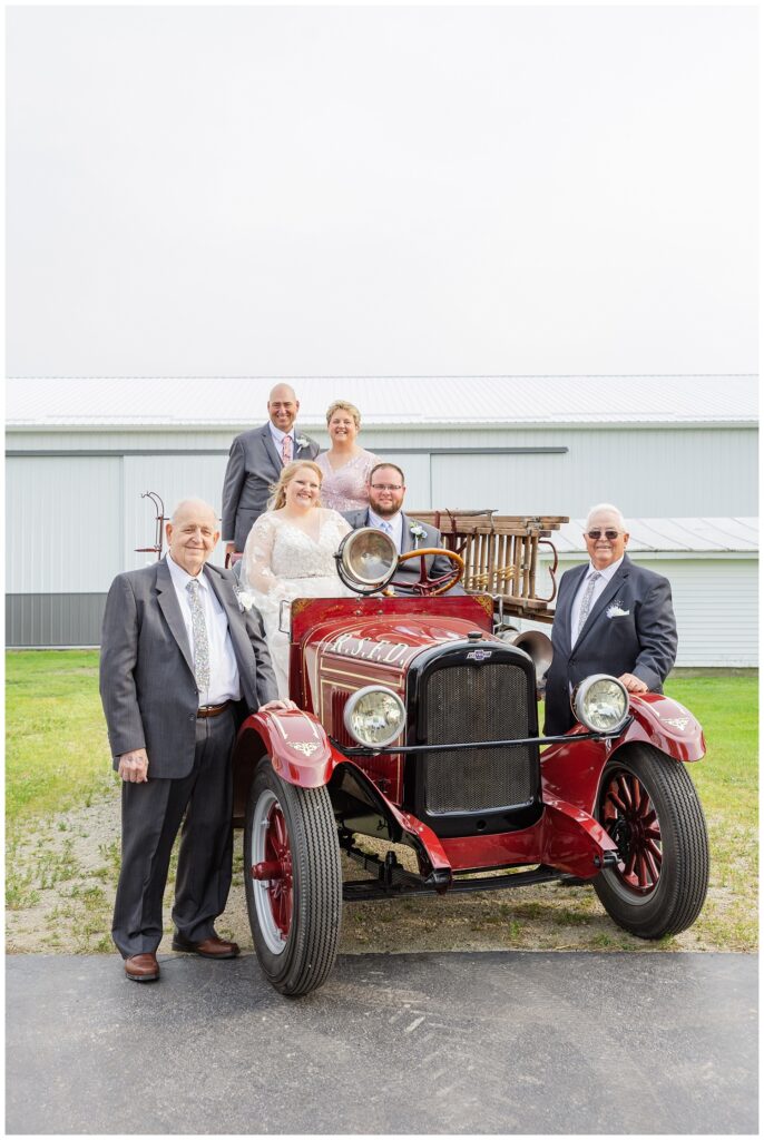 bride and groom's family posing around a red vintage fire truck at Ohio family farm