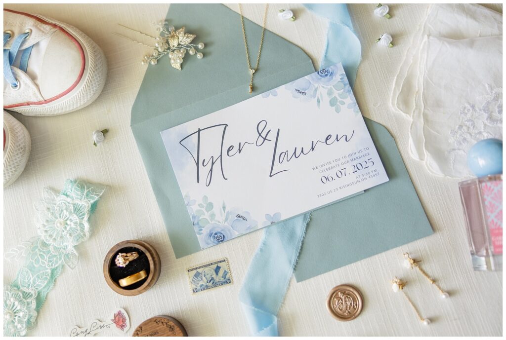 full wedding details with rings, invitation, earrings, shoes, and blue garter sitting on an ivory mat