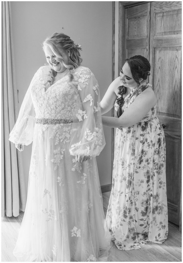 maid of honor buttoning the bride's dress from behind while getting ready