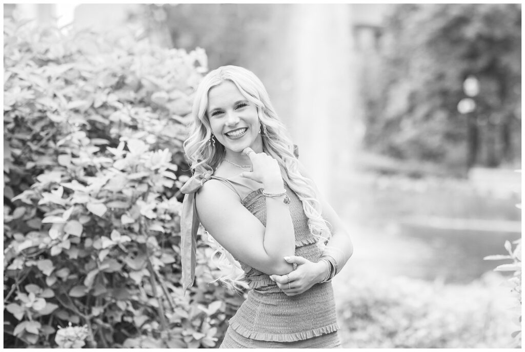 senior girl smiling next to a bush at the lake at Ohio State campus in Columbus