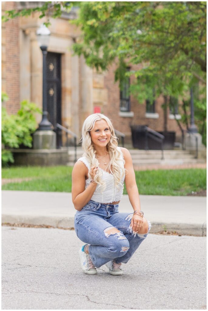 senior girl squatting on the street wearing a white top and jeans in Columbus, Ohio